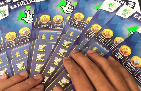 Close-up of several blue UK National Lottery scratchcards fanned out in two hands, showing the crossed-fingers logo and £4 million top prize text.