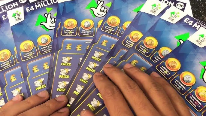 Close-up of several blue UK National Lottery scratchcards fanned out in two hands, showing the crossed-fingers logo and £4 million top prize text.